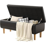 Black upholstered bench with storage compartment containing pillows, a blanket, and books on a white background