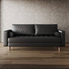 Black leather sofa in a room with wooden flooring and a textured wall.