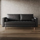 Black leather sofa in a room with wooden flooring and a textured wall.