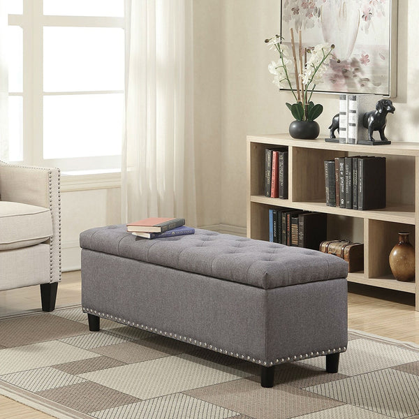 Gray tufted ottoman in a living room setting with books and decor items.