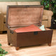 Brown storage trunk with cushions on a wooden floor, beige sofa in the background