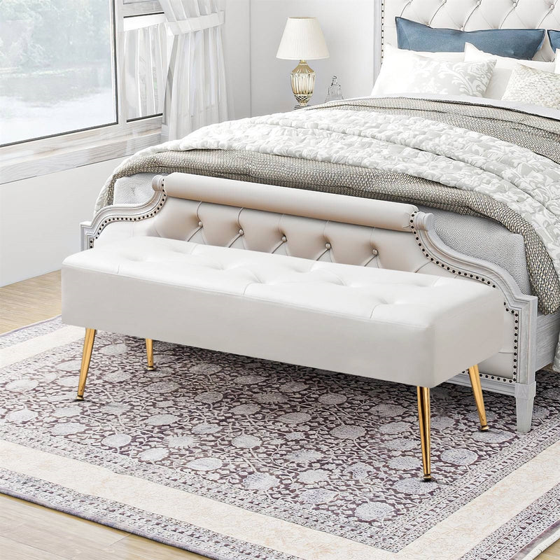 Beige tufted bench with gold legs in a bedroom setting