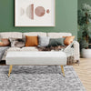 Living room with a beige sofa, white ottoman, and decorative pillows against a green wall.