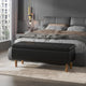 Black upholstered bench in front of a gray bed in a modern bedroom.